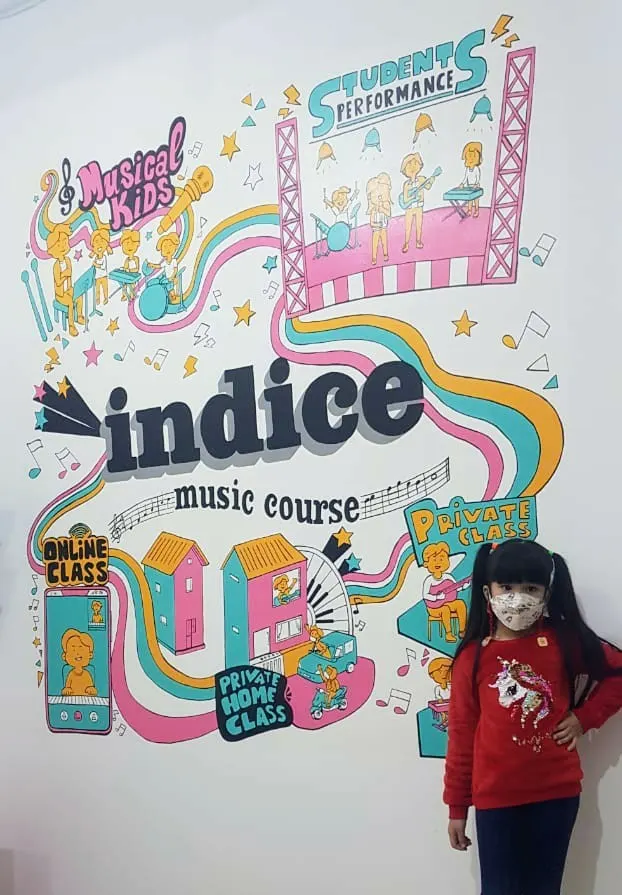 Murid cilik Indice berpose di depan mural Musical Kids