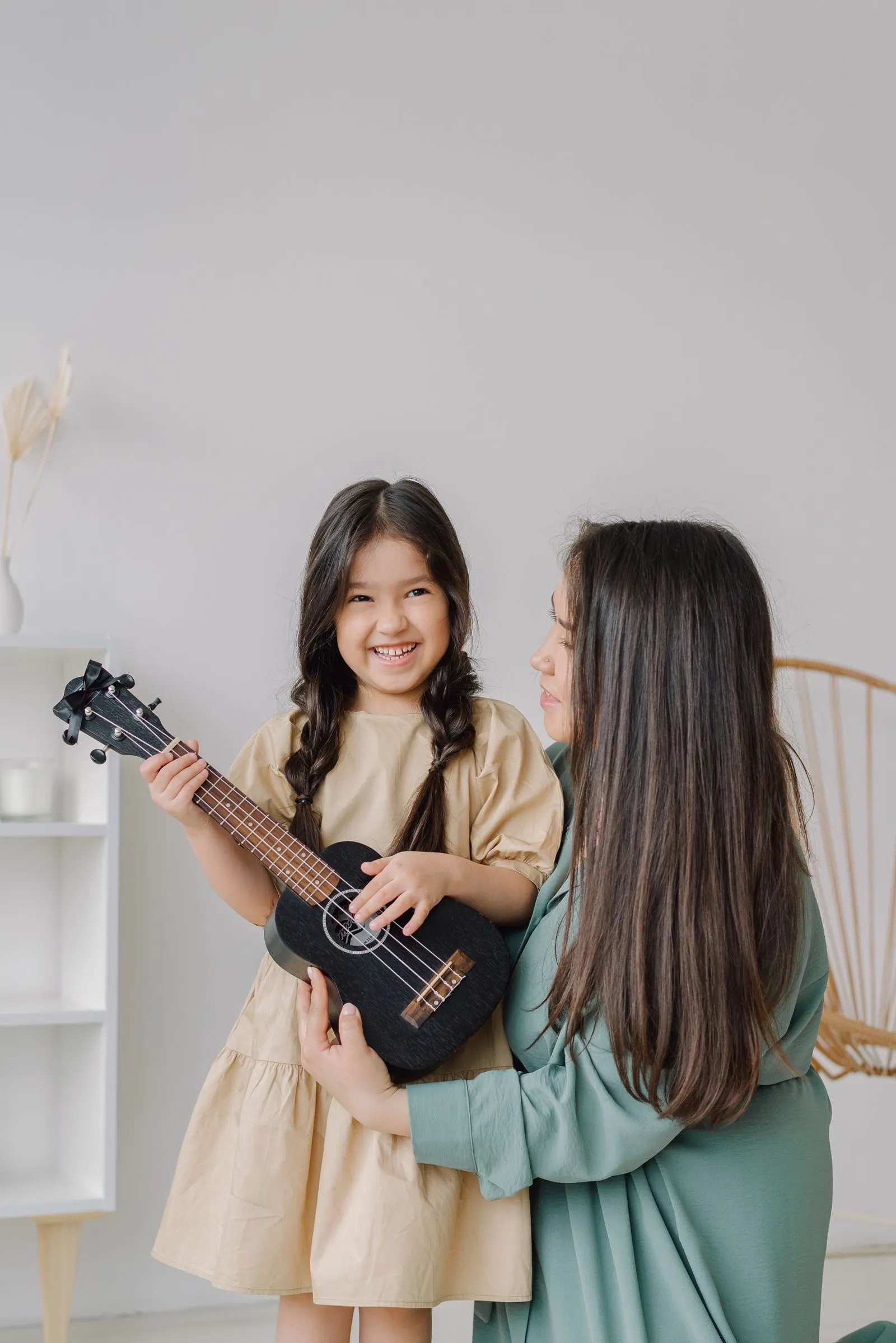 Anak perempuan tersenyum belajar ukulele didampingi pengajar