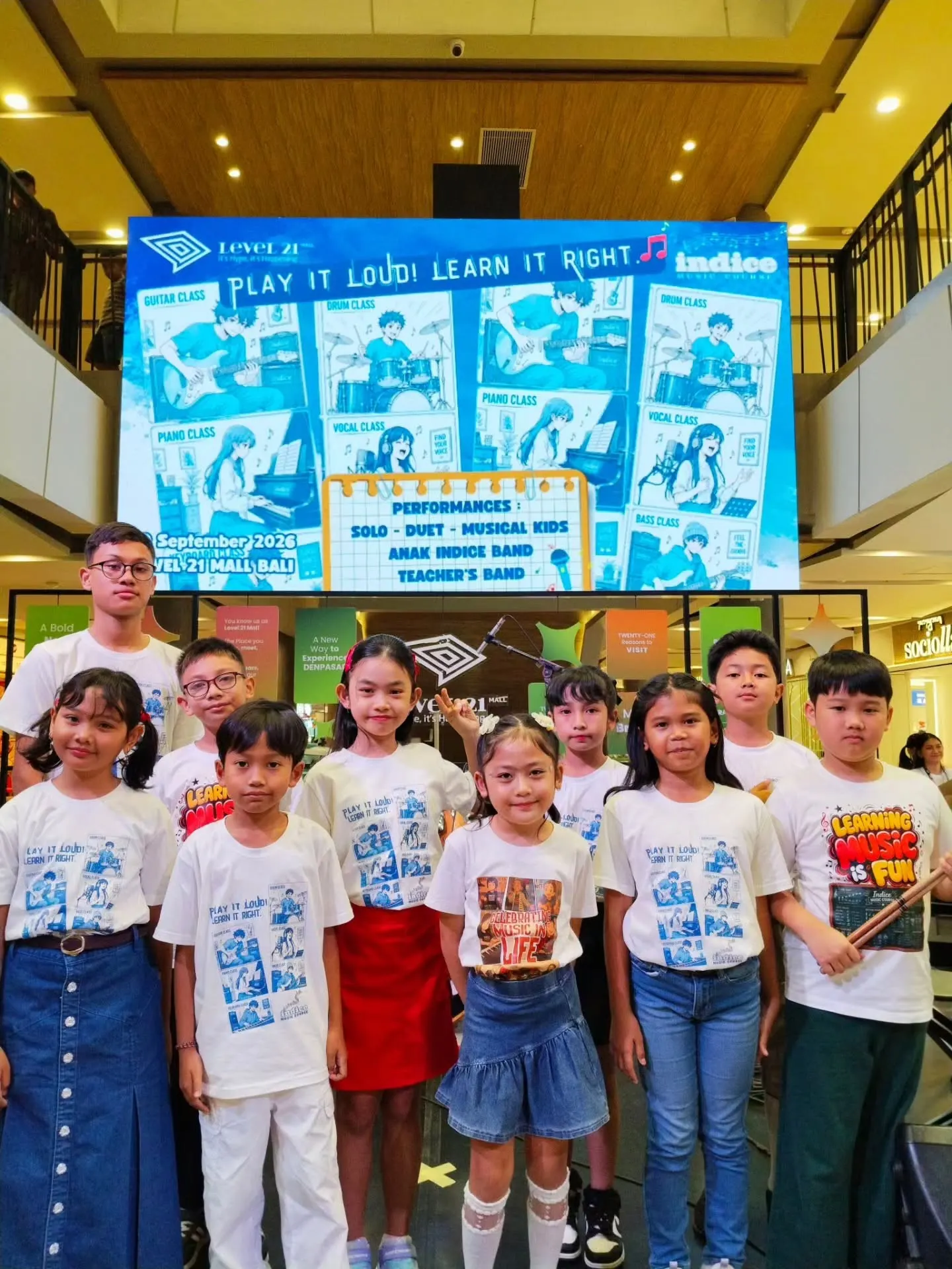 Murid-murid Indice berfoto di depan layar Student Performances Vol. 42 di Level 21 Mall